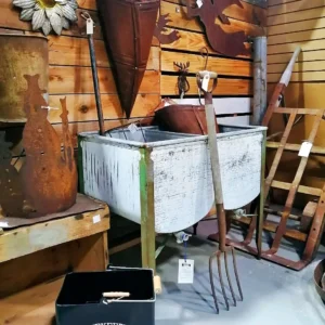 Vintage galvanized metal double wash tub on a green stand with an antique wooden-handled pitchfork.