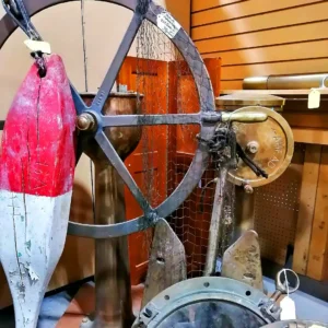 Collection of antique nautical decor featuring a large ship's wheel, a red and white wooden buoy, and a brass ship's telegraph.