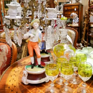 Antique porcelain figurine of a man in 18th-century attire posed next to yellow-tinted etched crystal glassware.