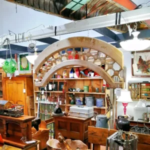 Ornate antique wooden architectural arch or valance displayed above shelves of vintage fishing and outdoor gear.