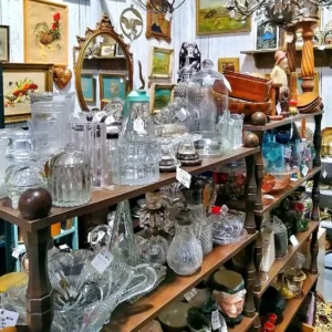 Organized shelves featuring a variety of clear pressed glass pitchers, storage jars, and decorative cloches.