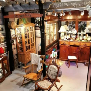 Interior of the Glastonbury-Glass booth featuring antique wooden cabinets, rocking chairs, and vintage lighting.