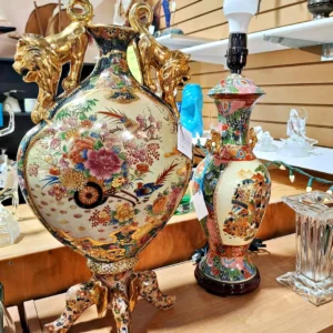 Pair of ornate Japanese Satsuma-style porcelain vases featuring intricate floral scenes and prominent gold-finished lion handles.