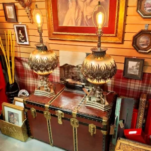 Pair of ornate gold-finished lamps with decorative floral patterns resting on a vintage leather-bound steamer trunk.