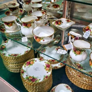 Close-up of vintage Royal Albert "Old Country Roses" patterned teacups and gold-rimmed plates in a glass display case.