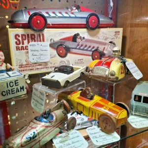 Vintage tin-litho toy race cars, featuring a boxed Schylling Spiral Race Car and other friction-powered collectibles on a shelf.