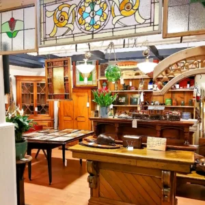 Rustic antique booth featuring hanging stained glass panels, a large wooden merchant counter, and fresh red tulips.