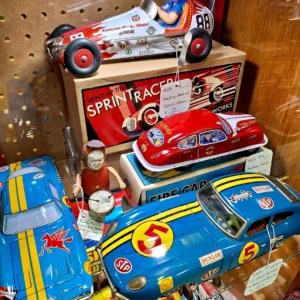 Close-up of vintage tin-litho toy cars featuring a boxed Schylling Sprint Racer and a blue Jaguar racing car.