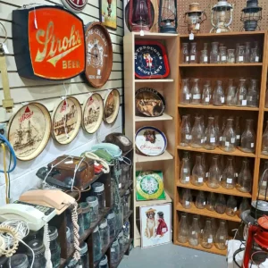 Display of vintage clear glass milk bottles alongside retro advertising signs for Stroh's Beer and Bass Ale.
