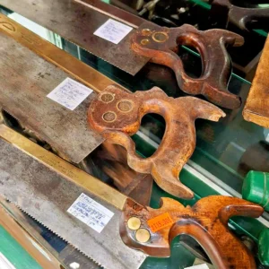 Close-up of vintage brass-back tenon saws and dovetail saws with ornate wooden handles and price tags.
