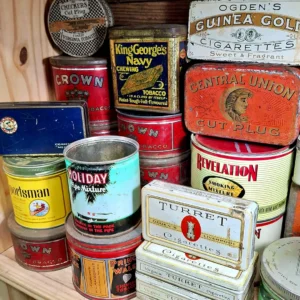 Stack of vintage advertising tins for tobacco and cigarettes, including brands like King George's Navy, Crown, and Turret.