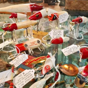 Assortment of vintage red and white wooden fishing lures with metal hooks and original price tags in a glass display case.