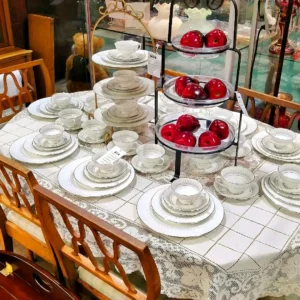 Formal dining table set with white and silver-rimmed china and a tiered server holding red decorative apples.
