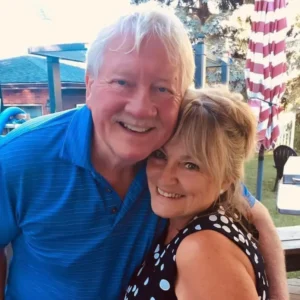 Henry Jones with his arm around Jackie, both smiling outdoors on a bright day.