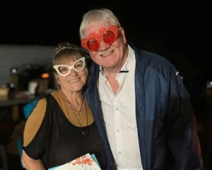 Henry Jones and Jackie wearing fun novelty heart and cat-eye glasses at a nighttime event.