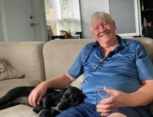 Henry Jones relaxing on a sofa with a small black dog sleeping soundly beside him.