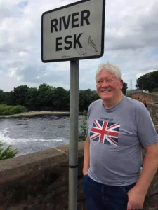 Henry Jones wearing a Union Jack t-shirt, standing by a "River Esk" sign on a bridge.