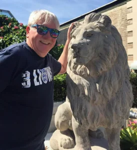 Henry Jones smiling while standing next to a large stone lion statue outdoors.