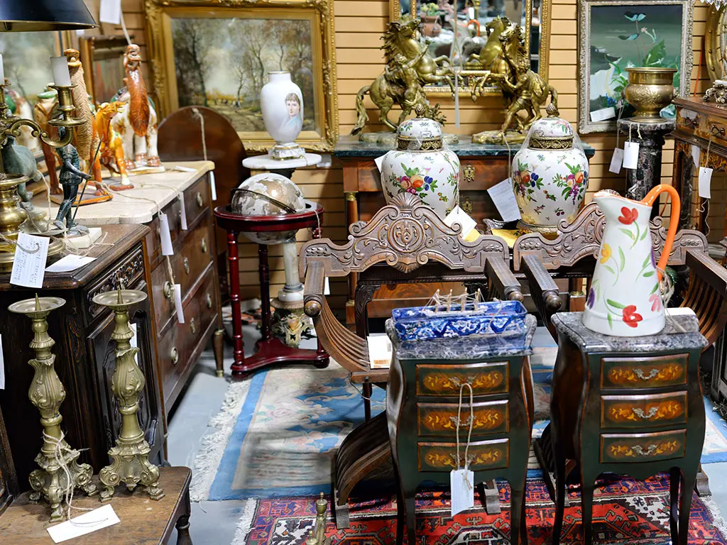 European antiques booth at Roadshow Antiques Mall showcasing ornate ginger jar porcelain, large bronze horse sculptures, carved furniture, antique globes, brass candlesticks, Oriental rugs, and oil paintings