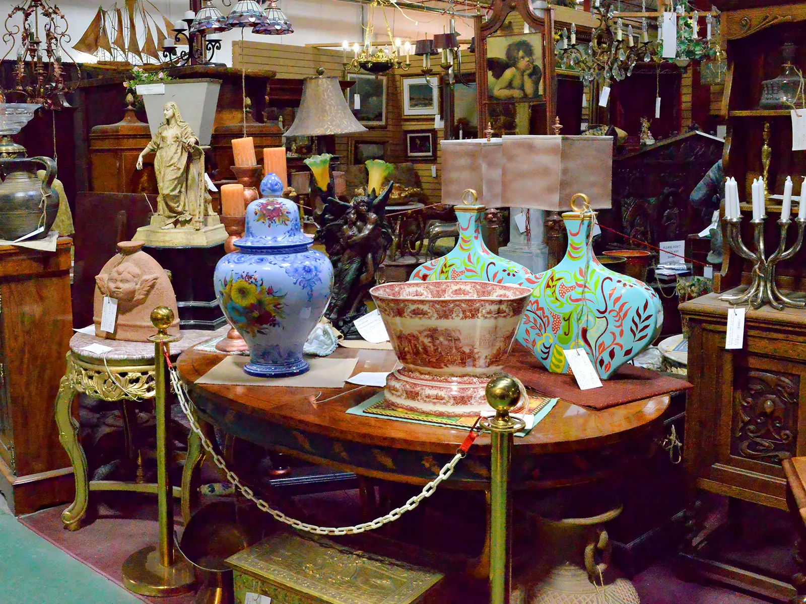 Colourful antique collectibles displayed at Roadshow Antiques Mall including a hand-painted blue ginger jar, turquoise decorative vases, a red transferware bowl, bronze sculptures, vintage lamps, and ornate furniture